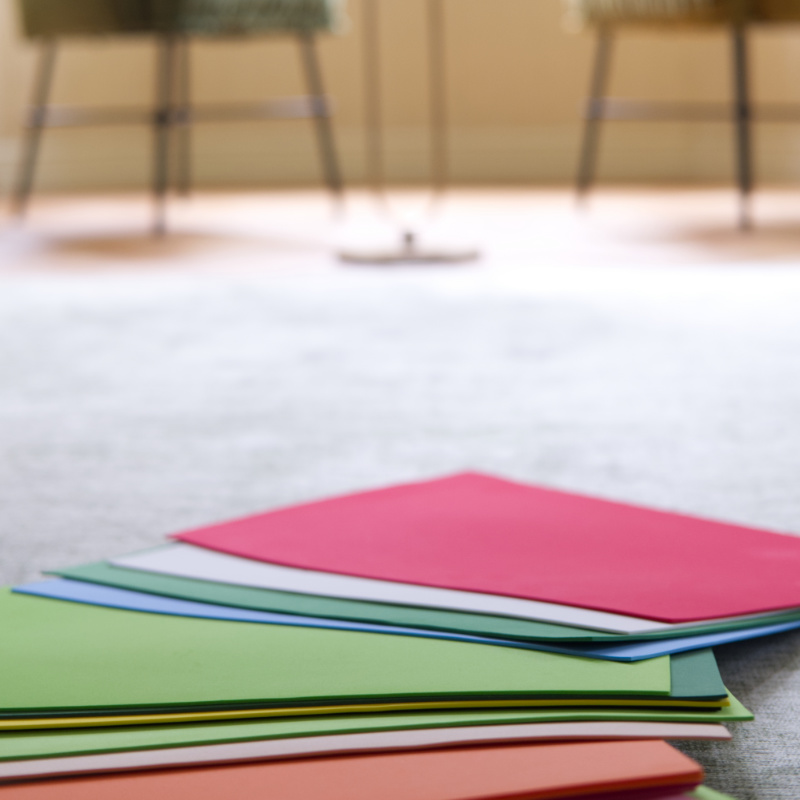 Eine Nahaufnahme eines Stapels bunter Filzkarten oder Blätter, die als Symbole für die systemische Aufstellungsarbeit auf einer hellgrauen Oberfläche verwendet werden